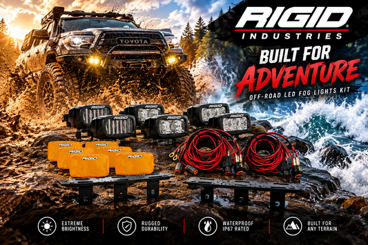 Rigid Industries Off-Road LED Fog Lights Kit displayed in front of a rugged off-road vehicle on a muddy trail, with the product components including orange fog lights, black light housings, red cables, and mounting brackets. The background shows a dramatic outdoor mountain scene with water and rocks.